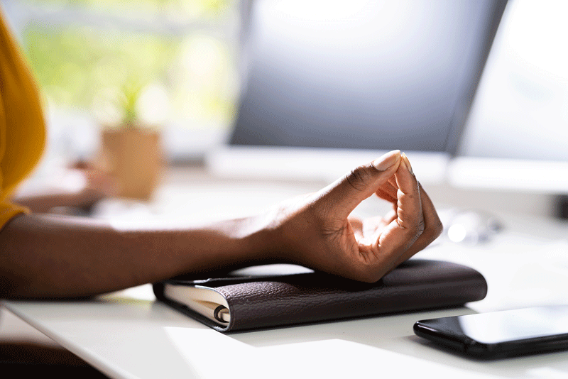 A close up of a person touching their index finger to their thumb in a meditative way while sitting at their work desk. This could represent a way to recharge at work and find personal fulfillment in Toronto, CA. Learn more about therapy for finding fulfillment in Ontario by contacting an Ontario, Canada therapist today.
